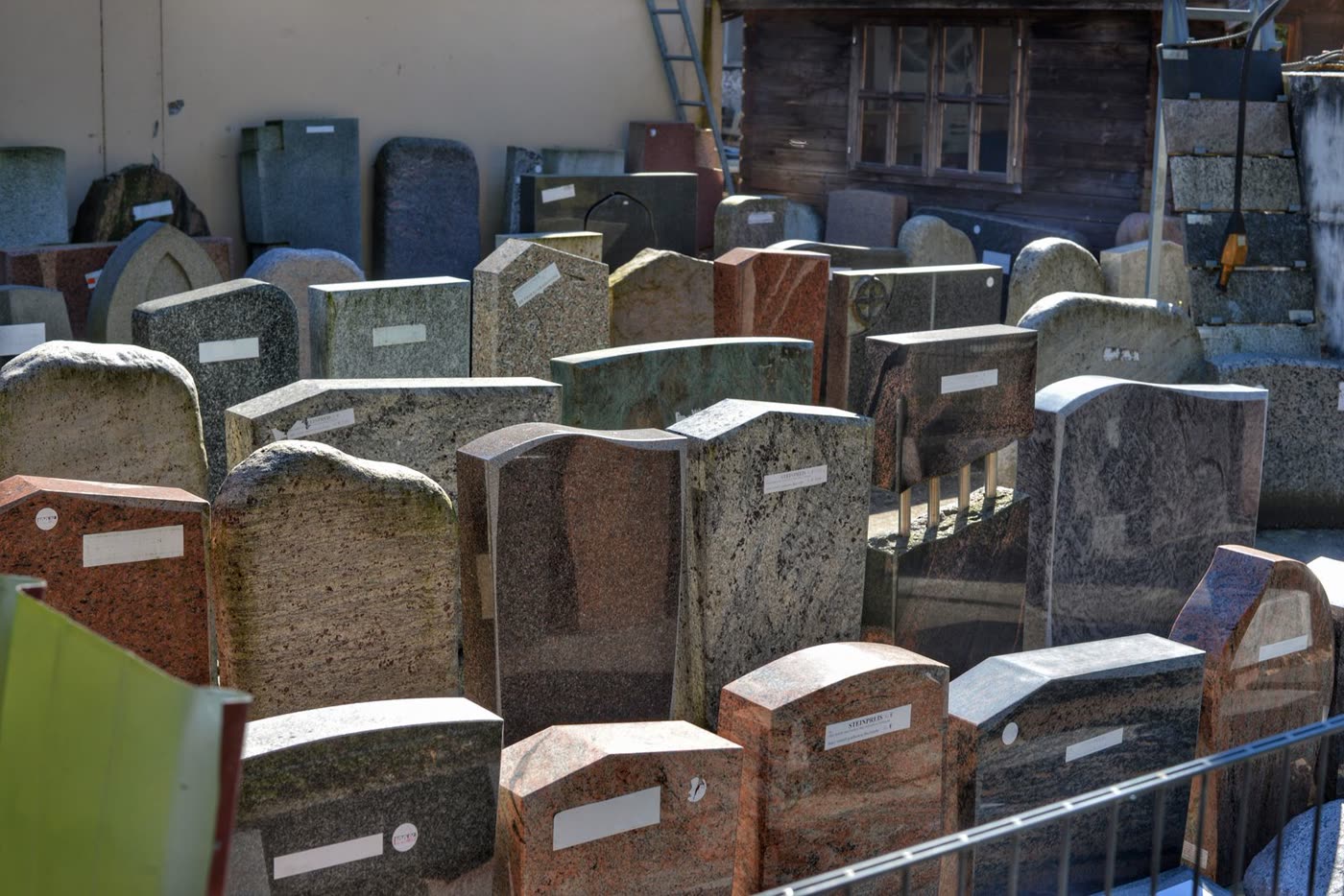 Dozens of upright granite headstones in gray, red, and black granite displayed outdoors at a monument dealer's showroom